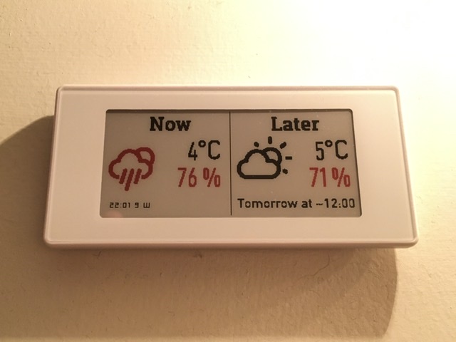 A rectangular e-paper display, the left half showing current weather and the right half showing upcoming rainy weather in red.