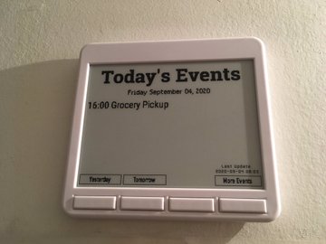 A square ePaper display mounted on a wall, showing a grocery pickup event at 16:00.